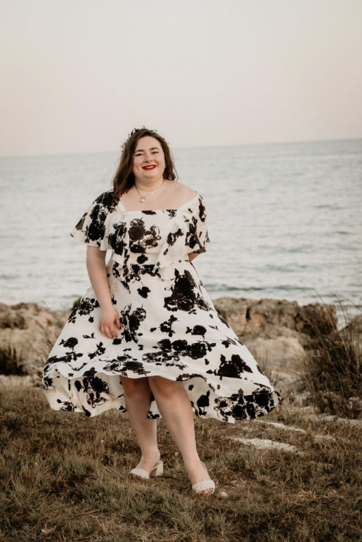 A young woman at a beach in a white dress with a black floral print